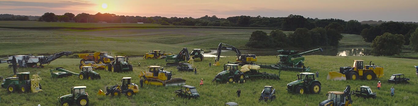 Personas caminando entre distintos equipos de John Deere en un gran campo.