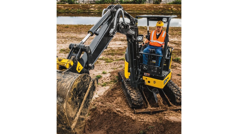 Un operador empleando una Excavadora 26P para recoger tierra en un lugar de trabajo con un estanque en el fondo.