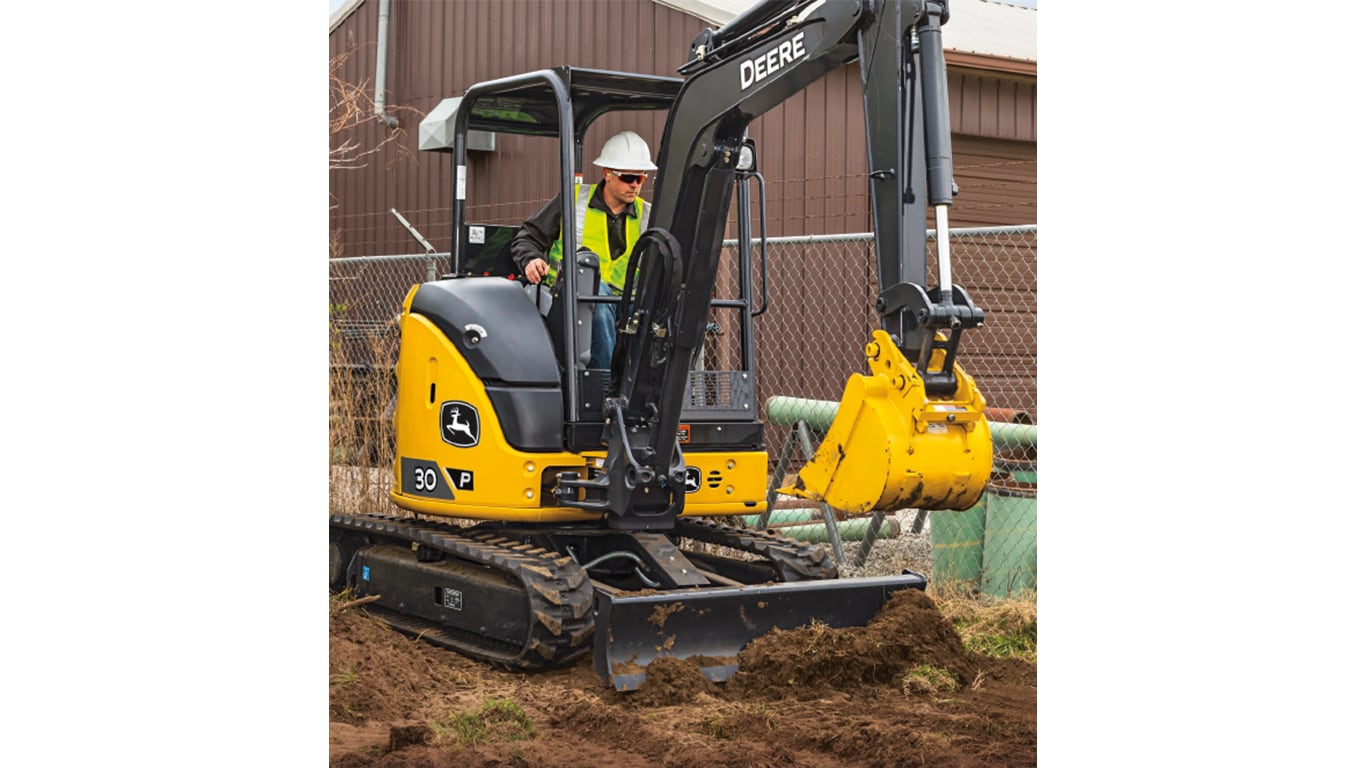 Un operador usa una Excavadora 30P-Tier para mover tierra en un lugar de trabajo con una cerca y un edificio café en el fondo.