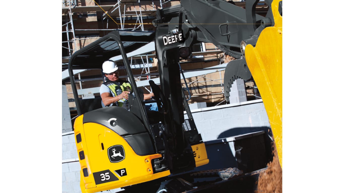 Primer plano de un operador que usa una Excavadora 35P-Tier para mover tierra en un lugar de trabajo con la construcción del edificio en el fondo.