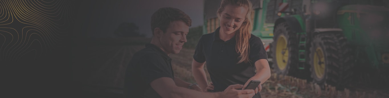 Imagen de un hombre sosteniendo su teléfono móvil junto a una mujer, la cual observa cómo éste utiliza la aplicación John&nbsp;Deere Operations Center.