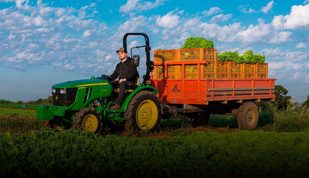 Una persona conduciendo un tractor John Deere a través de un campo.