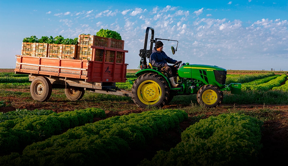 Una persona conduciendo un tractor John Deere a través de un campo.