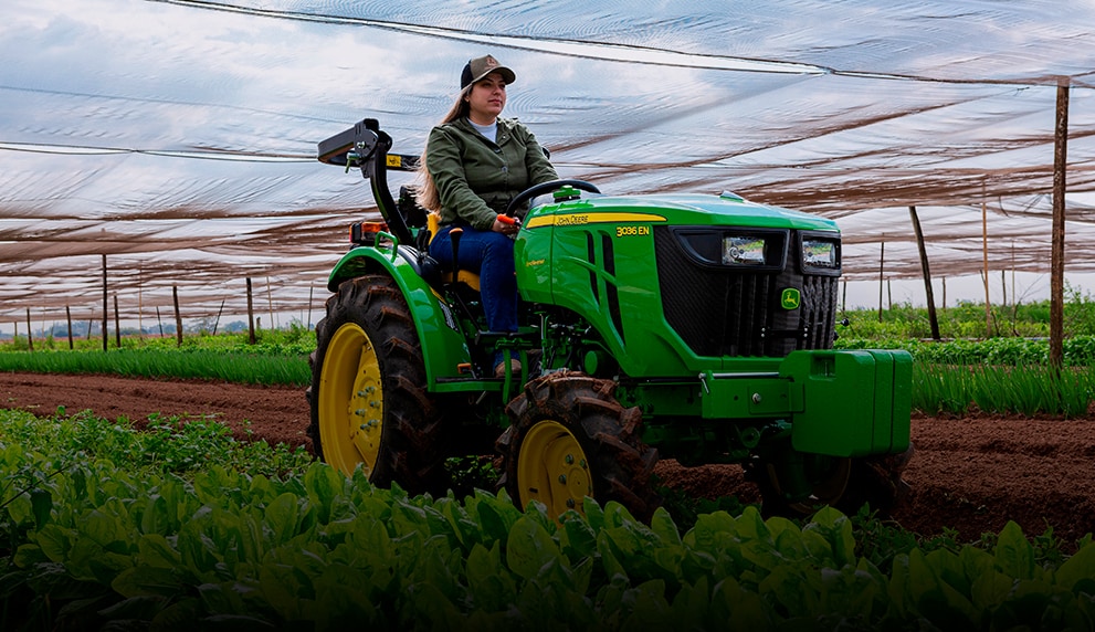 Una persona conduciendo un tractor John Deere a través de un campo.