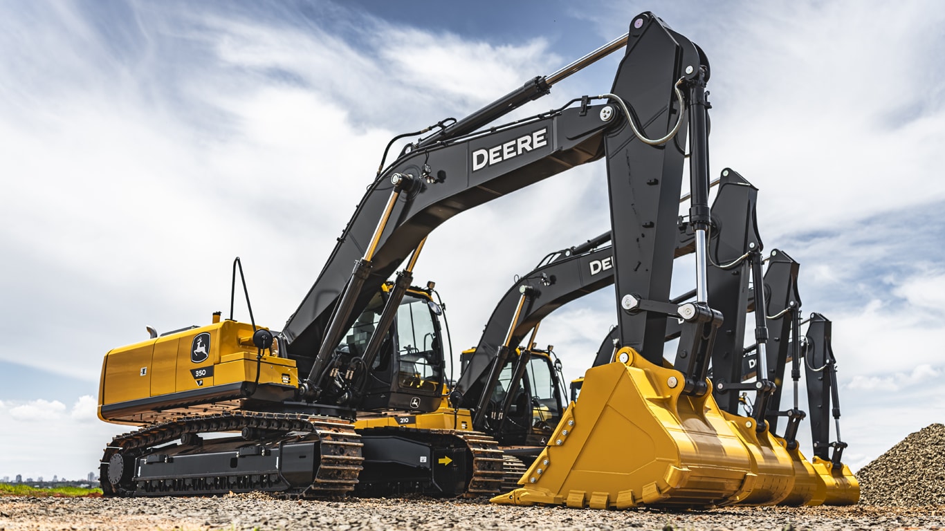Hilera de cuatro excavadoras medianas diferentes de Deere sobre grava.