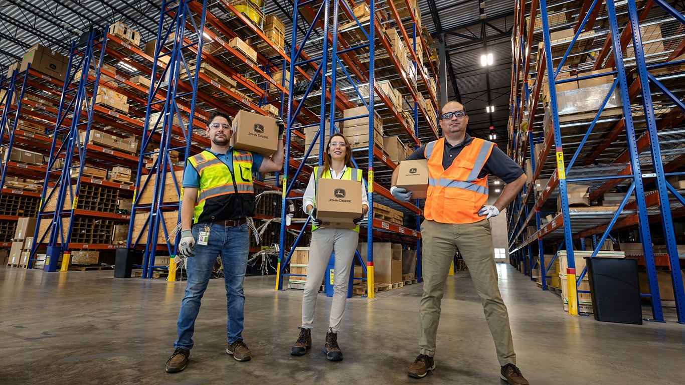 three employees holding boxes in front of warehouse steels
