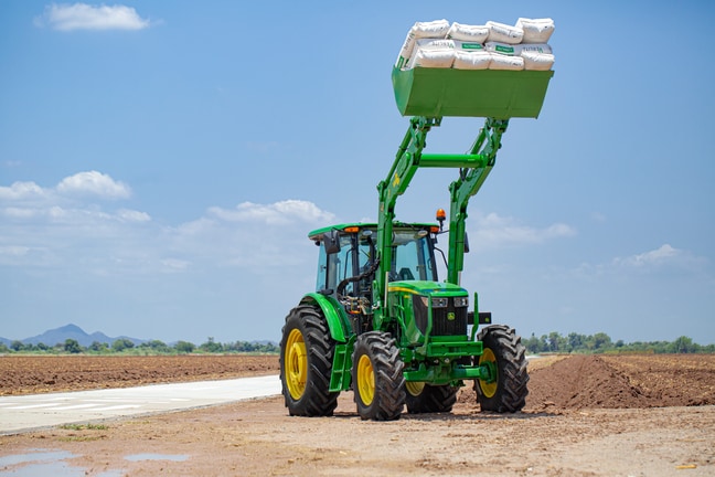 Imagen de tractor 6140E con cargador levantando sacos de tierra