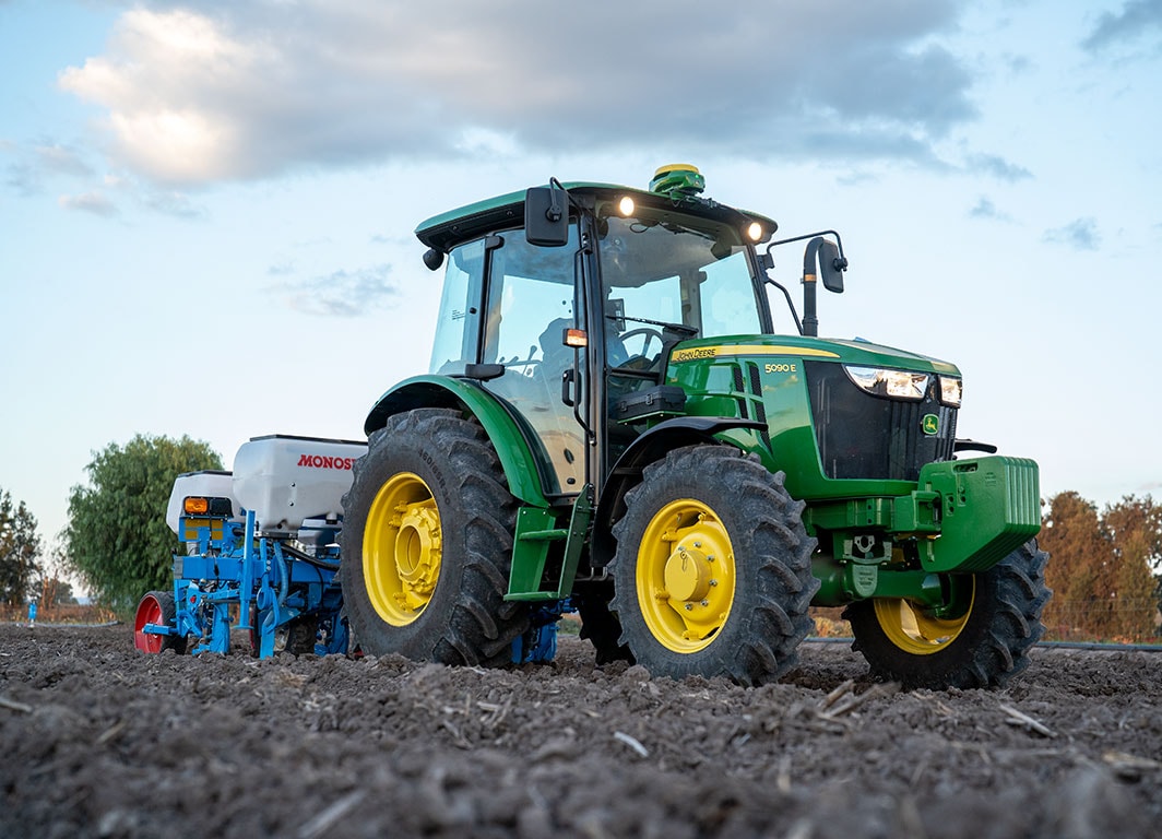 Tractor trabajando en un campo con sembradora Monosem, avanzando sobre suelo preparado al atardecer.