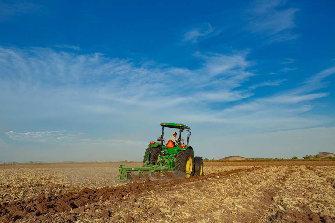 tractor 6120E trabajando con el suelo con rastra, visto desde atrás. Fndo de cielo azul con nubes blancas.