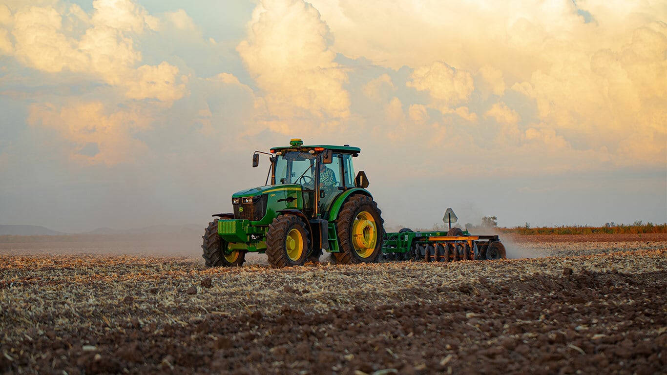 tractor 6803 trabajando en un campo con implemento de arado con un cielo de atardecer de fondo