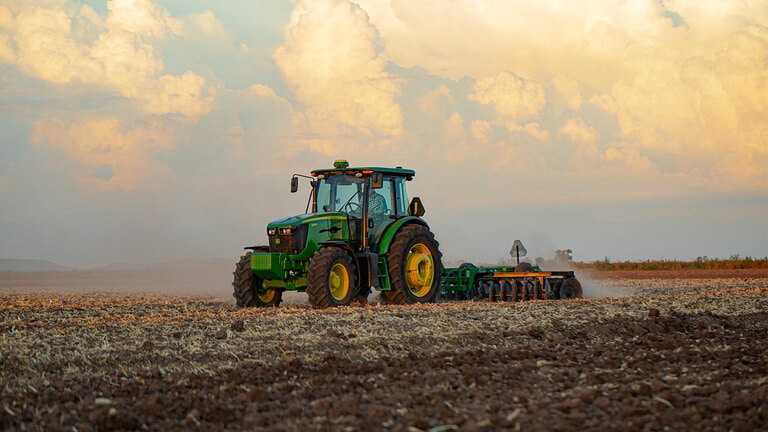 tractor 6803 trabajando en un campo con implemento de arado con un cielo de atardecer de fondo