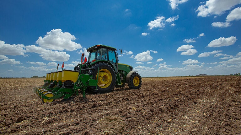 tractor 6803 avanzando con sembradora, es manejado por un técnico con sombrero, hay un fondo de cielo azul con algunas nubes blancas